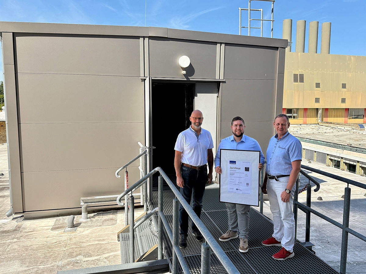 Klinikumsdirektor André Koch, Energiemanager Fabian Lange und Technischer Leiter Michael Braune stehen auf einem Klinikdach; Fabian Lange hält das gerahmte Zertifikat.