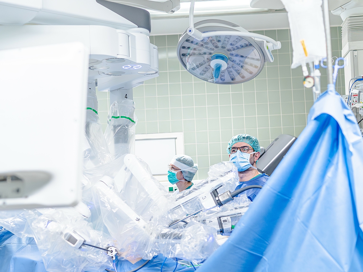 Ein chirurgisches Team steht in einem Operationssaal, das einen Roboterarm für eine Operation bedient. Die Ärzte tragen medizinische Schutzkleidung und konzentrieren sich auf die Arbeit unter sterilem Umfeld.